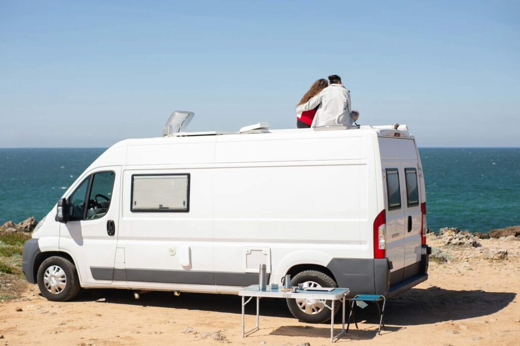 Young Couple sitting on top of a campervan by the sea in Spain